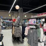 Luminarias lineales LED cruzadas y focos de carril para iluminación comercial en zona de ropa.