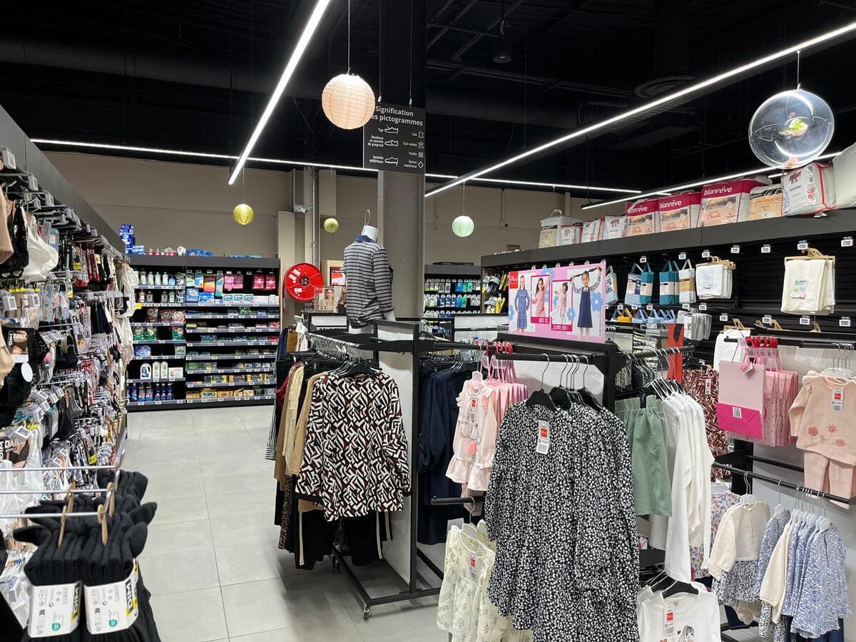 Luminarias lineales LED cruzadas y focos de carril para iluminación comercial en zona de ropa.