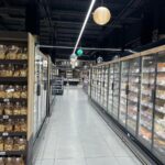 Iluminación suspendida decorativa y funcional en pasillo lateral del supermercado.