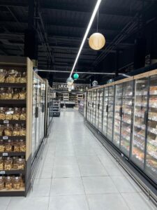 Iluminación suspendida decorativa y funcional en pasillo lateral del supermercado.
