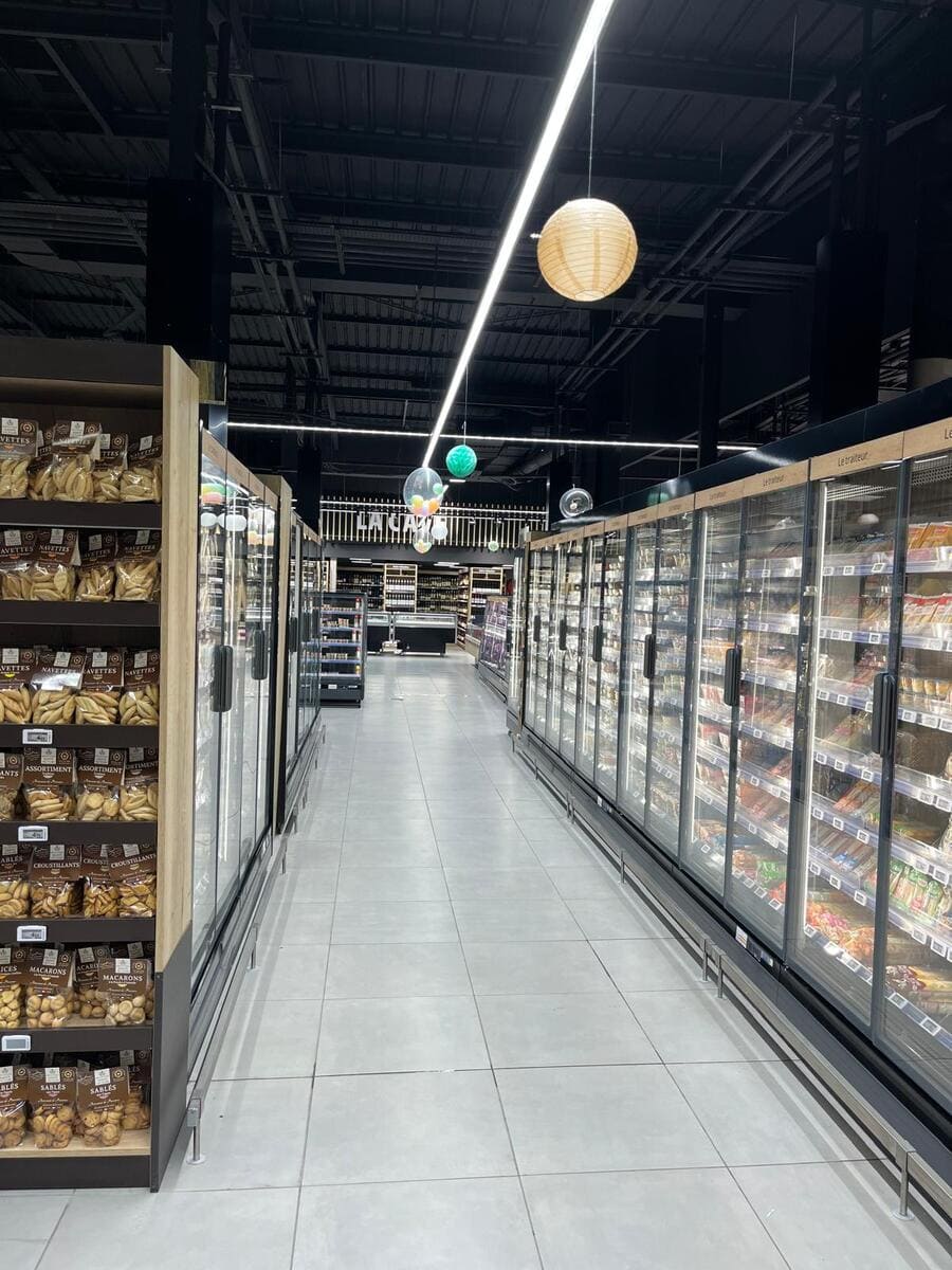 Iluminación suspendida decorativa y funcional en pasillo lateral del supermercado.